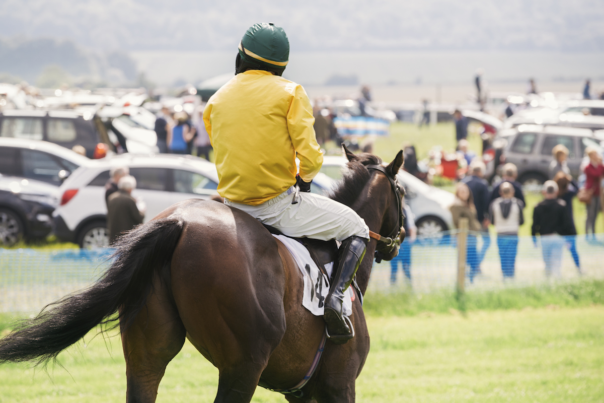 jockey in yellow and green silks riding a bay horse